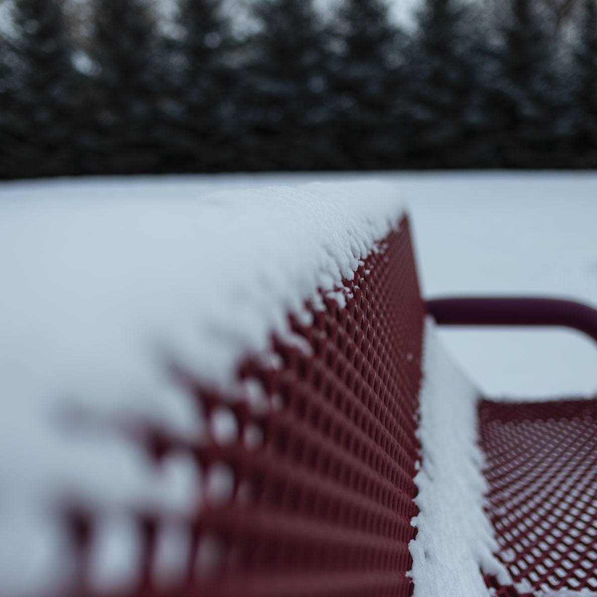 A snow covered park bench is almost completely blurred using a shallow depth-of-field except for the focus point halfway through the image.