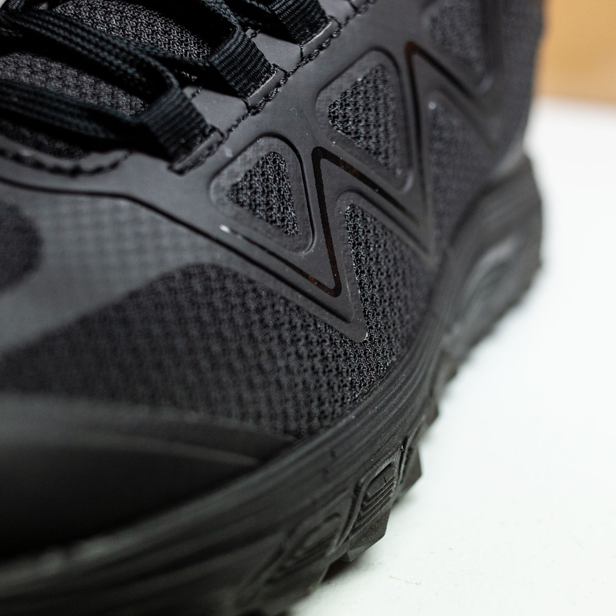 This image of Bates Footwear mid Rush on a white background also uses low angle and shallow depth-of-field to give the subject power and highlight the attractive design of this all black, athletic style running shoe.