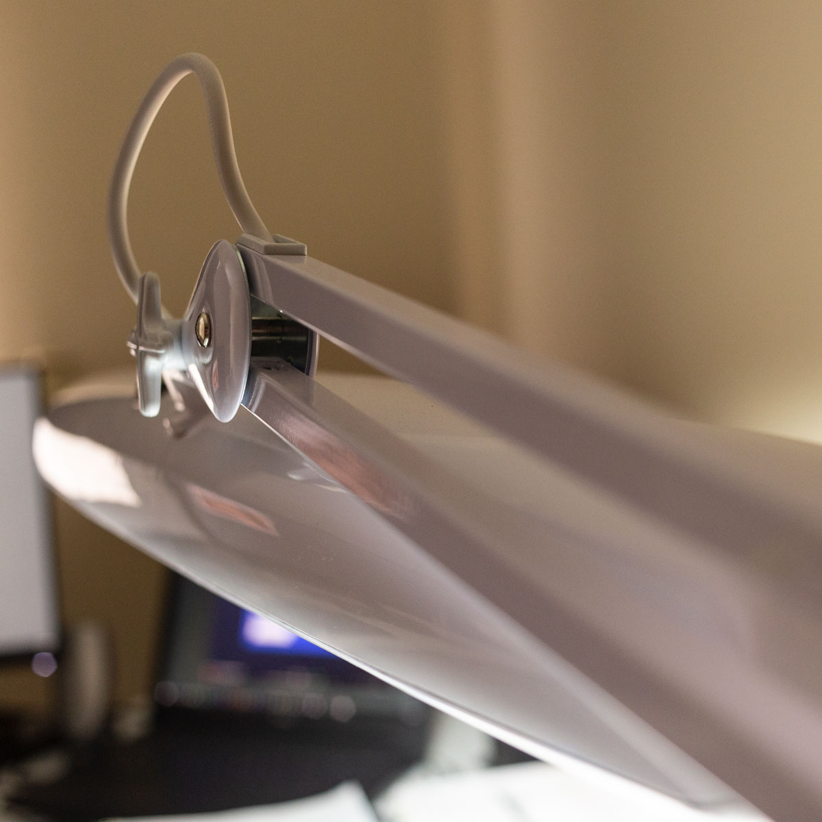 A close-up image of a desk lamp showing the twin tubes of it's support arm leading in to the lamp adjustment screw.