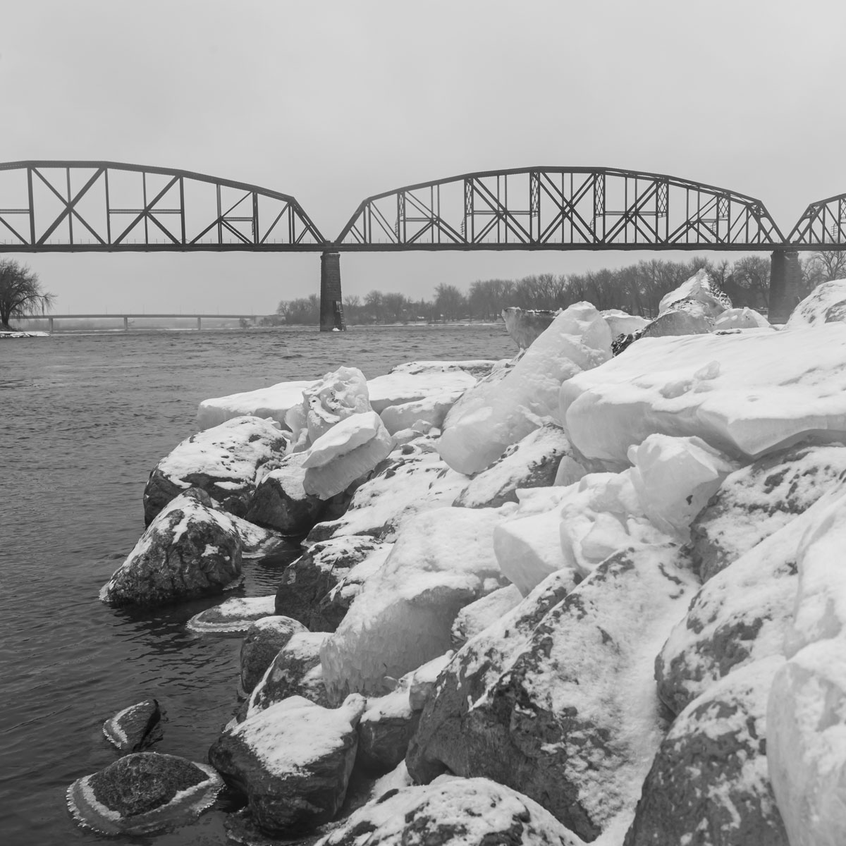 In this image of large chunks of ice and rocks beside the Missouri River on a clouldy, cold and misty day a low perspective of the ice leads the way to a railroad bridge in the background. The low perspective draws the viewer to the ice giving it power and leads the viewer into the background. 