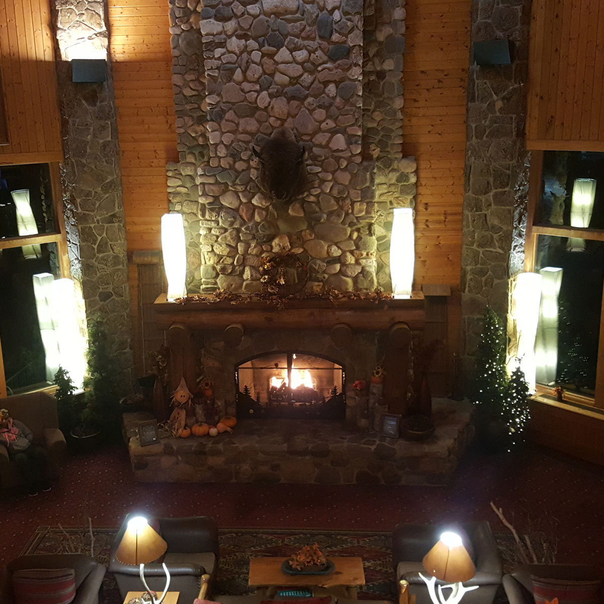 The warmth of a fire blazes from a stone hearth and chimney in a lobby of pine walls trimmed in stone at Spearfish Canyon Lodge on a cool October night. Comfortable leather chairs are lit by lamps made of deer antlers. An Autumn arrangement of pumpkins and scarecrows line the hearth in the warm light of fireplace and lamps.