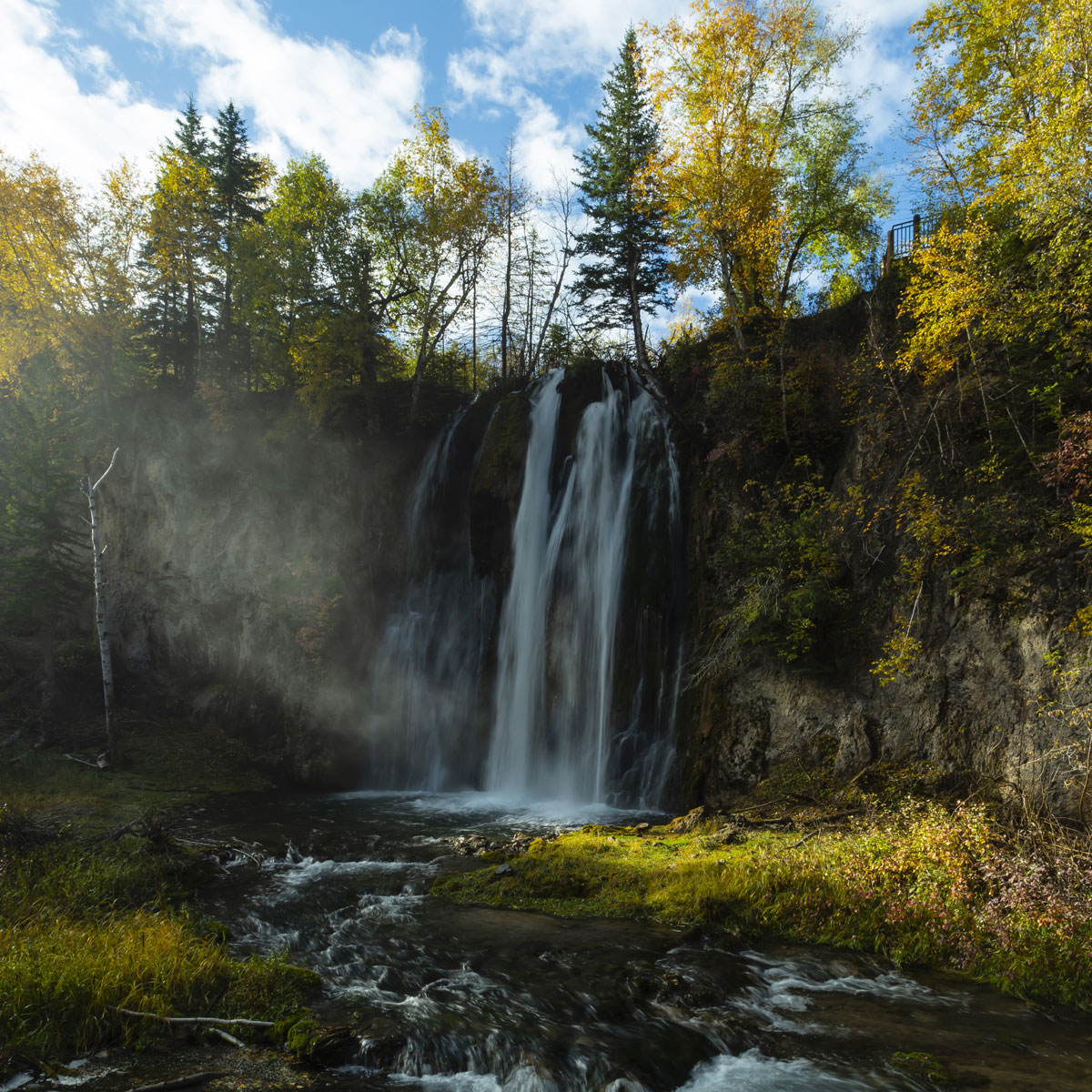 The waters of Spearfish Falls spill into the pools below with a silvery mist lit by an early morning sun.